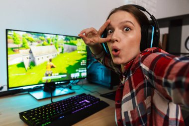 Heyecanlı kız oyun oturma masada bir selfie alarak online oyun kapalı, bir bilgisayarda oynamak