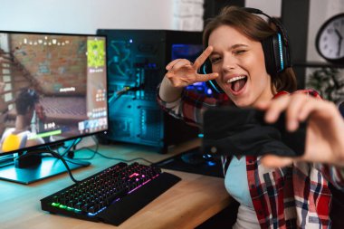 Heyecanlı kız oyun oturma masada bir selfie alarak online oyun kapalı, bir bilgisayarda oynamak