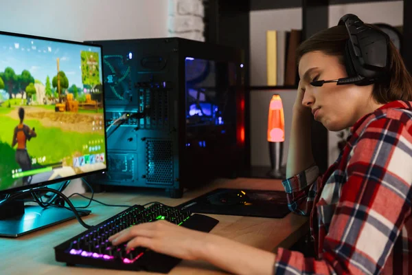 Bilgisayar oyunları oynarken masada oturan kulaklıklar giyen genç bir kadın portresi