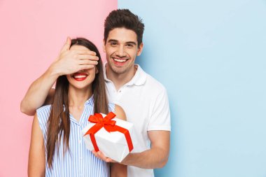 Mutlu genç çift ayakta kutluyor, hediye kutusu tutan iki renkli arka plan, izole