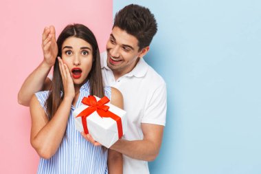 Mutlu genç çift ayakta kutluyor, hediye kutusu tutan iki renkli arka plan, izole