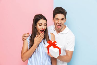 Mutlu genç çift ayakta kutluyor, hediye kutusu tutan iki renkli arka plan, izole