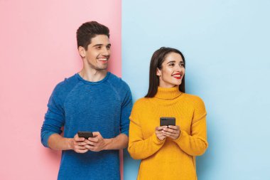 Genç çift ayakta tutan cep telefonları iki renkli arka plan izole