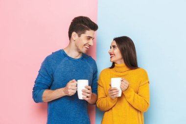 Güzel genç çift ayakta iki renkli arka plan, holding bardak çay ile izole.
