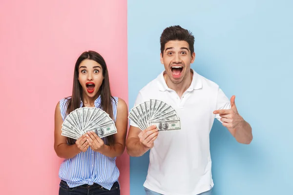 兴奋的年轻夫妇站在两个彩色的背景隔离 显示货币钞票 — 图库照片
