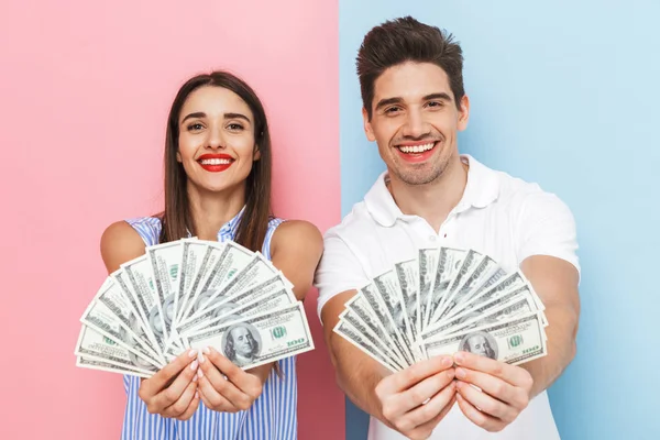 兴奋的年轻夫妇站在两个彩色的背景隔离 显示货币钞票 — 图库照片