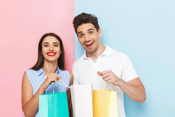 Happy Young Couple Standing Isolated Two Colored Background Carrying Shopping — Stock Photo, Image