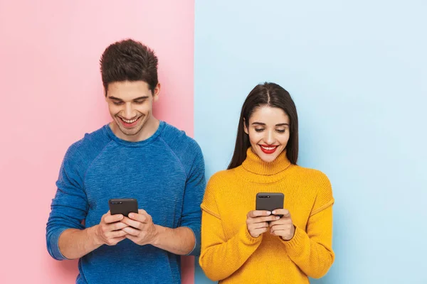 陽気な若いカップルの立っている分離された 色の背景 保有携帯電話 — ストック写真