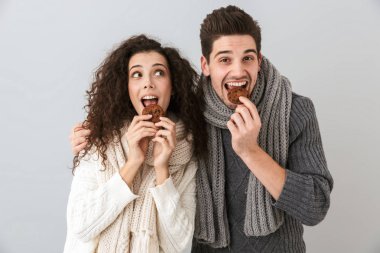 Çekici çift erkek ve gri arka plan üzerinde izole kurabiye yemek tulum giyen kadın fotoğrafı
