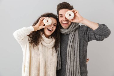 Kazak ve donuts gösterilen gri arka plan üzerinde izole ayakta tulum giyen genç çift