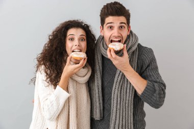 Kazak ve donuts gösterilen gri arka plan üzerinde izole ayakta tulum giyen genç çift