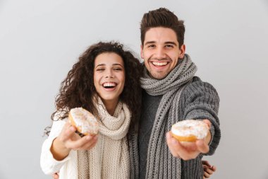 Kazak ve donuts gösterilen gri arka plan üzerinde izole ayakta tulum giyen genç çift
