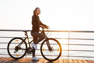 Sağlıklı kadın binicilik bisiklet üzerinde tahta deniz üzerinde gündoğumu sırasında fotoğraf