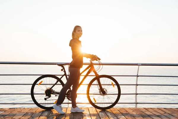 日出时女性与自行车站在木板路上的照片 — 图库照片