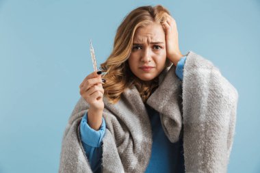 Mavi arka plan üzerinde izole termometre tutan battaniyeye sarılmış görüntü hasta genç kadının 20'li