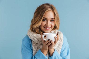 Sevimli kadın 20'li yaşlarda görüntü gülümseyen ve fincan çay veya kahve üzerinde mavi arka plan izole tutan eşarp sarılı