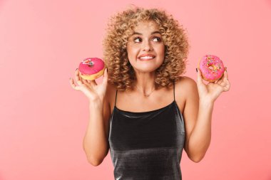 Sırlı donut yemek neşeli genç kadın kıvırcık saçlı pembe arka plan üzerinde izole ayakta