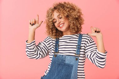 Glamour kıvırcık kadın 20'li yaşlarda fotoğrafı üzerinde pembe arka plan izole dans ederken gülümseyen