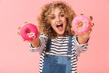 Glamour kıvırcık kadın 20'li yaşlarda giyiyor rahat kıyafetler donuts pembe arka plan üzerinde izole ayakta süre tutarak fotoğrafı