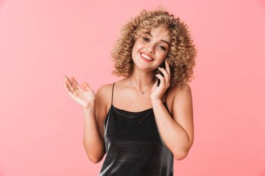 Sevimli kıvırcık kadın 20'li yaşlarda portresi gülümseyen ve cep telefonu pembe arka plan izole konuşurken