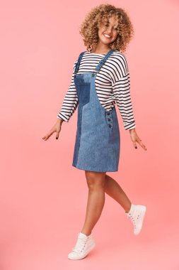 Tam boy görüntü muhteşem kıvırcık kadın 20'li yaşlarda giyiyor rahat kıyafetler üzerinde pembe arka plan izole iken gülümseyen