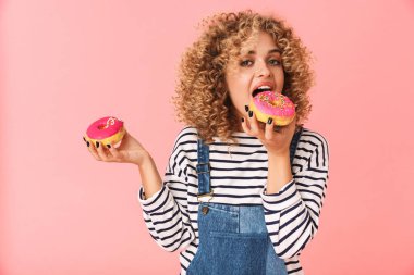 Sevimli kıvırcık kadın 20'li yaşlarda giyiyor rahat kıyafetler donuts pembe arka plan üzerinde izole ayakta süre tutarak fotoğrafı