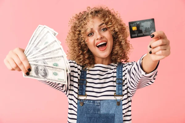 持美元和信用卡粉丝的高加索卷曲的妇女20多岁的照片 同时站在粉红色的背景隔离 — 图库照片