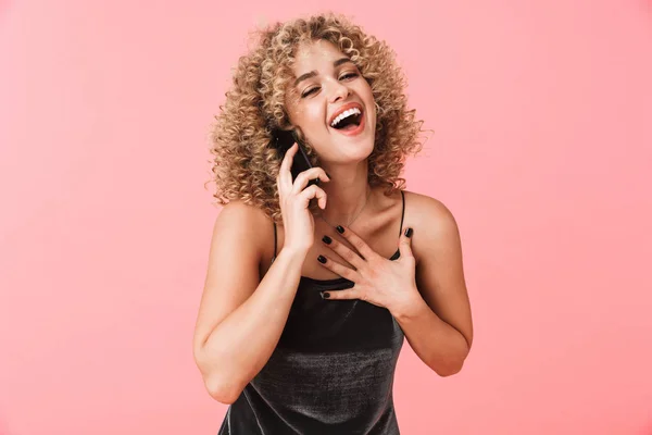 Portrait of glamorous curly woman 20s smiling and talking on mobile phone isolated over pink background