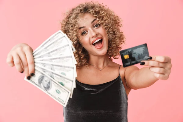 照片中的迷人卷曲的女人20多岁穿着礼服 穿着美元和信用卡的粉丝 而站在粉红色的背景孤立 — 图库照片