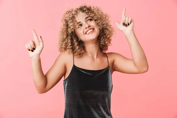 Portrait of beautiful curly woman 20s wearing dress dancing and smiling while isolated over pink background