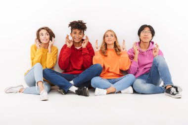 İyi şans getirmesi için parmak holding beyaz bitti, izole grup neşeli çok ırklı arkadaşıyla oturan geçti