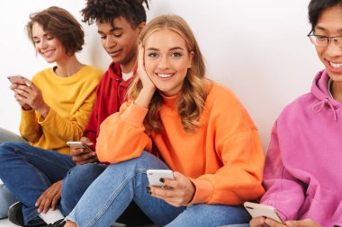 Cep telefonları holding beyaz bitti, izole grup neşeli çok ırklı arkadaşıyla oturan