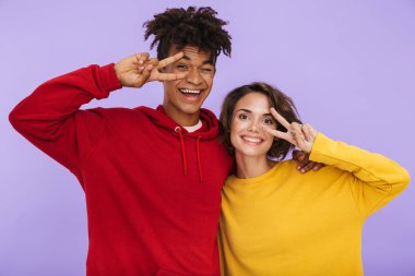 Neşeli multhiethnic genç çift ayakta birlikte barış gösterilen menekşe arka plan üzerinde izole