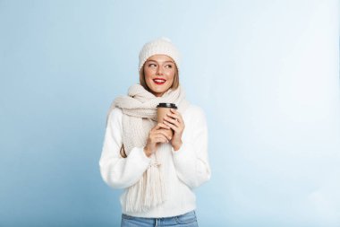 Paket servisi olan restoran kahve tutan kazak ve izole üzerinde mavi arka plan, şapkası giyen mutlu genç kadın