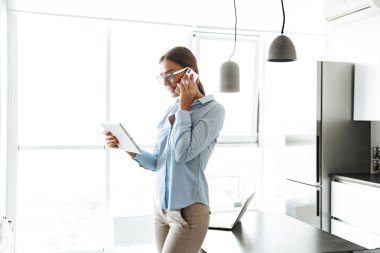 Gülümseyen genç işkadını cep telefonuyla duran bir mutfak