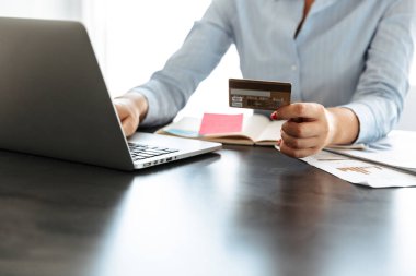 Plastik kredi kartı gösteren masada otururken dizüstü bilgisayarda çalışan bir işkadını yakın çekim