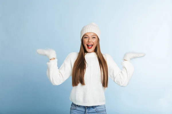 興奮した若い女性のセーターと帽子を身に着けている分離青い背景にコピー スペースを提示 — ストック写真