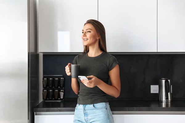 Happy Young Woman Standing Kitchen Drinking Tea Using Mobile Phone — Stock Photo, Image
