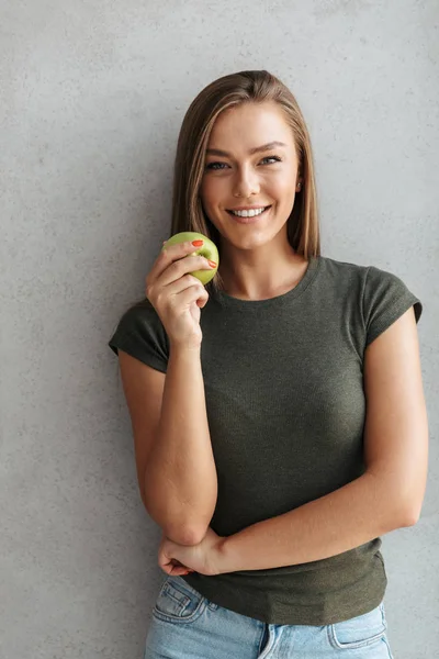 Vrolijke Jonge Vrouw Staande Aan Muur Thuis Bedrijf Groene Appel — Stockfoto