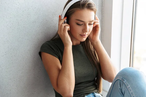 愉快的年轻女子在家用耳机听音乐 — 图库照片