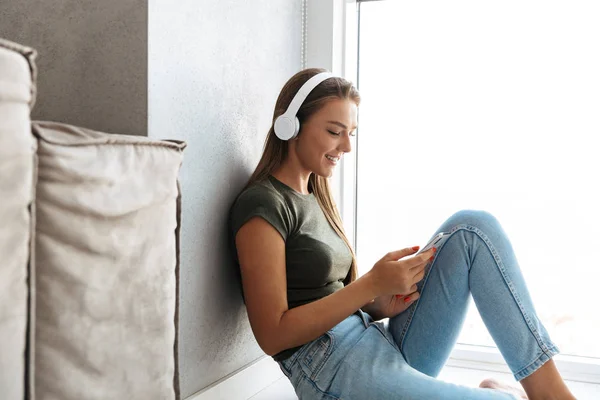 愉快的年轻女子在家用耳机听音乐 用手机 — 图库照片