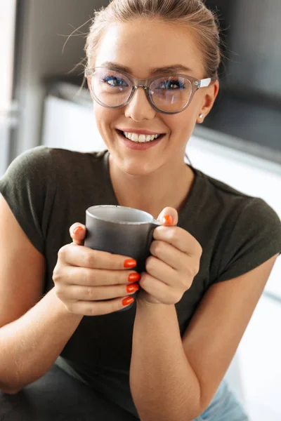 微笑的年轻女子坐在厨房里拿着杯子 — 图库照片