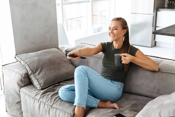 Cheerful Young Woman Sitting Couch Home Changing Channels Drinking Tea — Stock Photo, Image