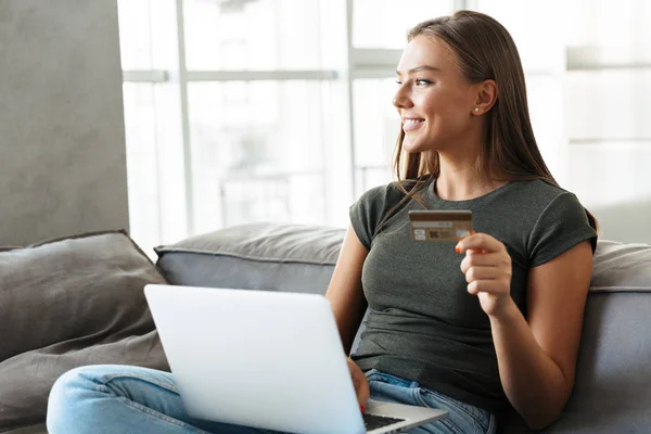 Mujer Joven Sonriente Sentada Sofá Casa Usando Ordenador Portátil Mostrando —  Fotos de Stock