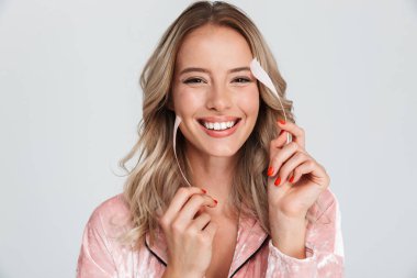 Güzel genç sarı saçlı kadın gri arka plan üzerinde izole, bir tüy ile vücuduna dokunarak