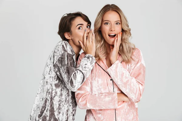 Sırlarını anlatmaya gri arka plan üzerinde izole pijama giymiş iki güzel kız