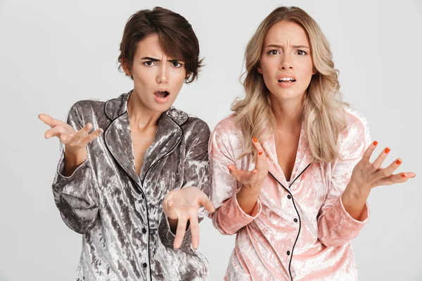 İki rahatsız kız pijama gri arka plan üzerinde izole ayakta giyiyor, kameraya bakarak