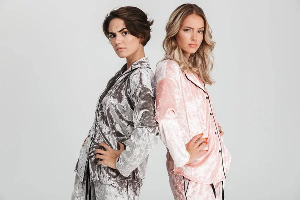 İki rahatsız kız pijama gri arka plan üzerinde izole ayakta giyiyor, kameraya bakarak