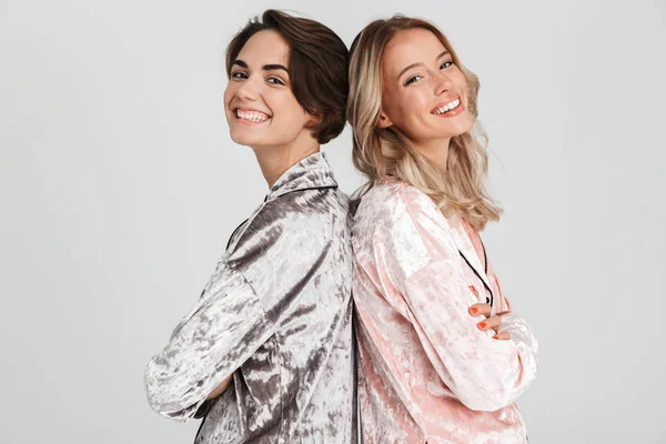 Sırt sırta duran gri arka plan üzerinde izole pijama giymiş iki güzel kız