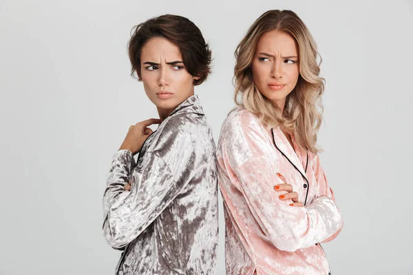 Sırt sırta duran gri arka plan üzerinde izole pijama giymiş iki üzgün kız